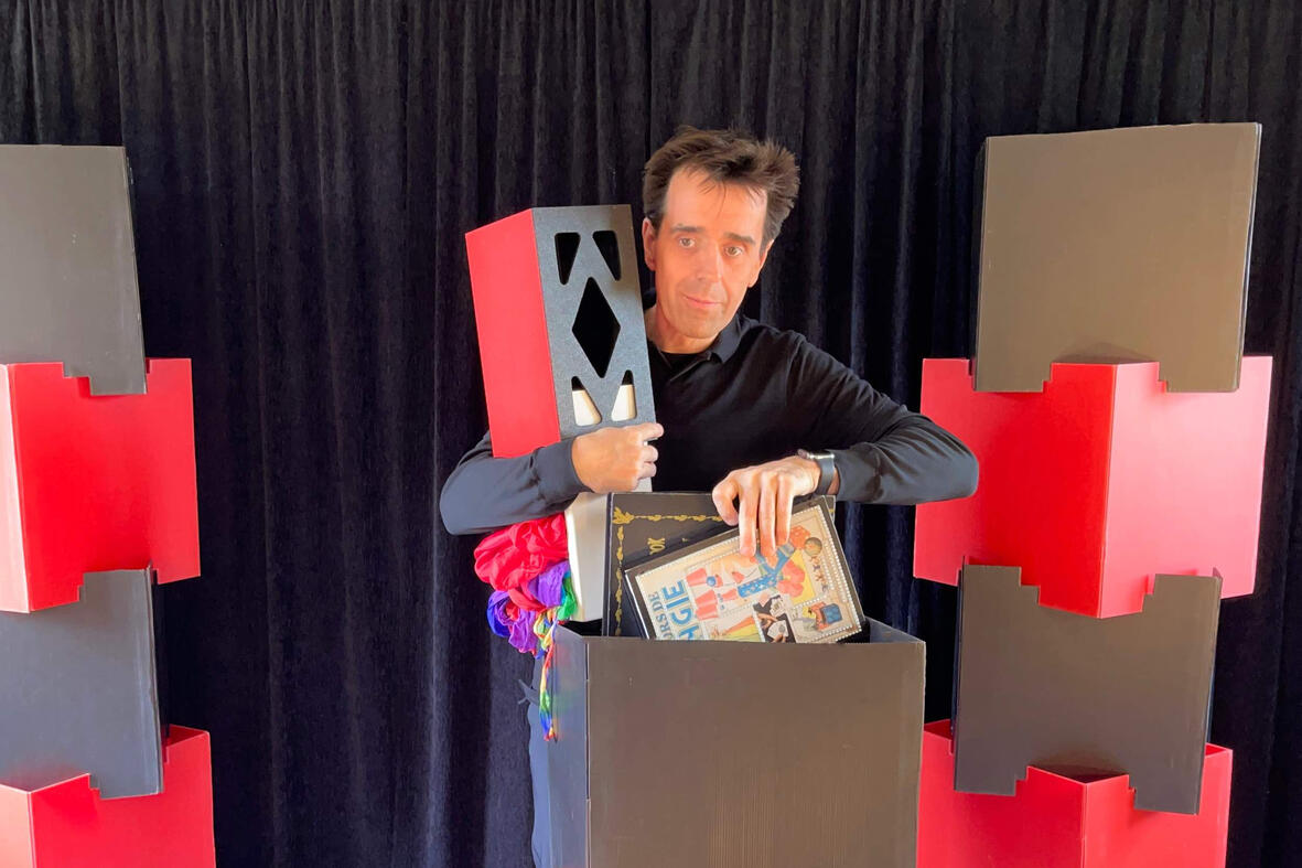 Monsieur Fred présente un livre magique et utilise une boîte pour faire apparaître des doudous sur scène, émerveillant le jeune public lors du spectacle