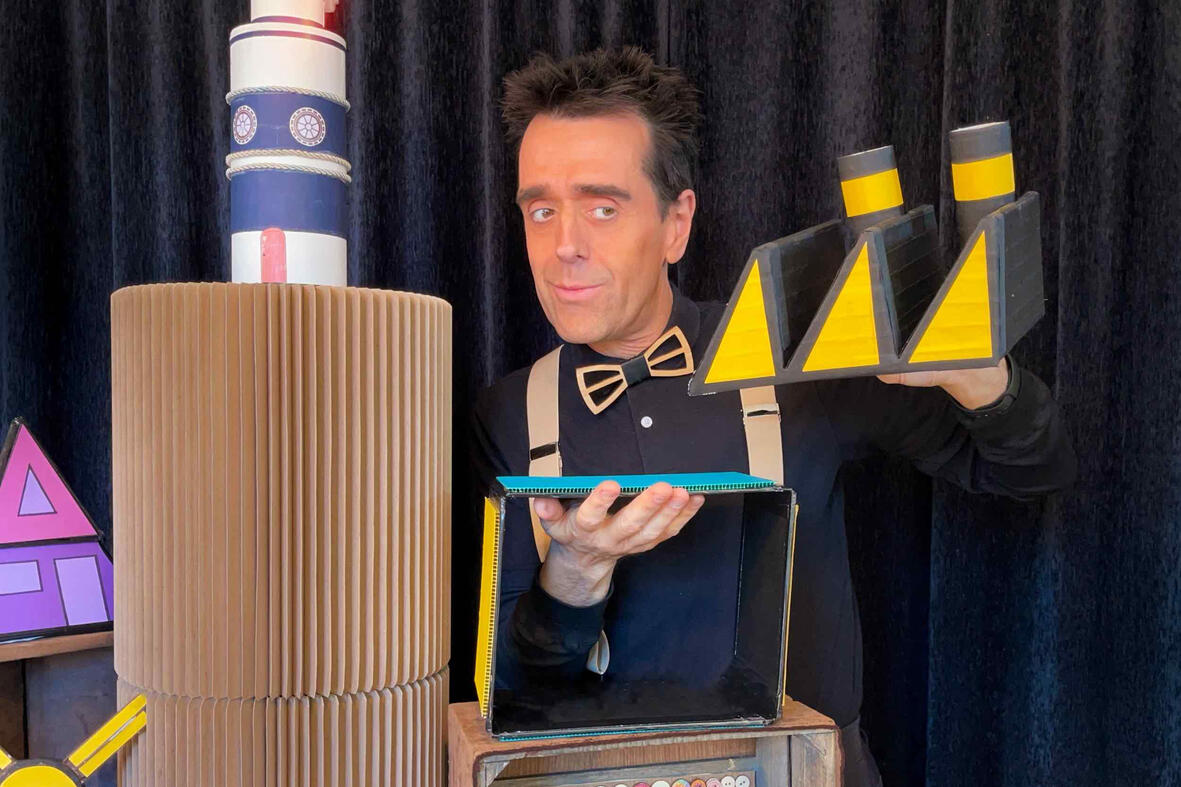 Risque-Tout Monsieur Fred en spectacle, entouré de l’univers de Risque-Tout avec le village, la maison et l’île, offrant des surprises aux enfants.