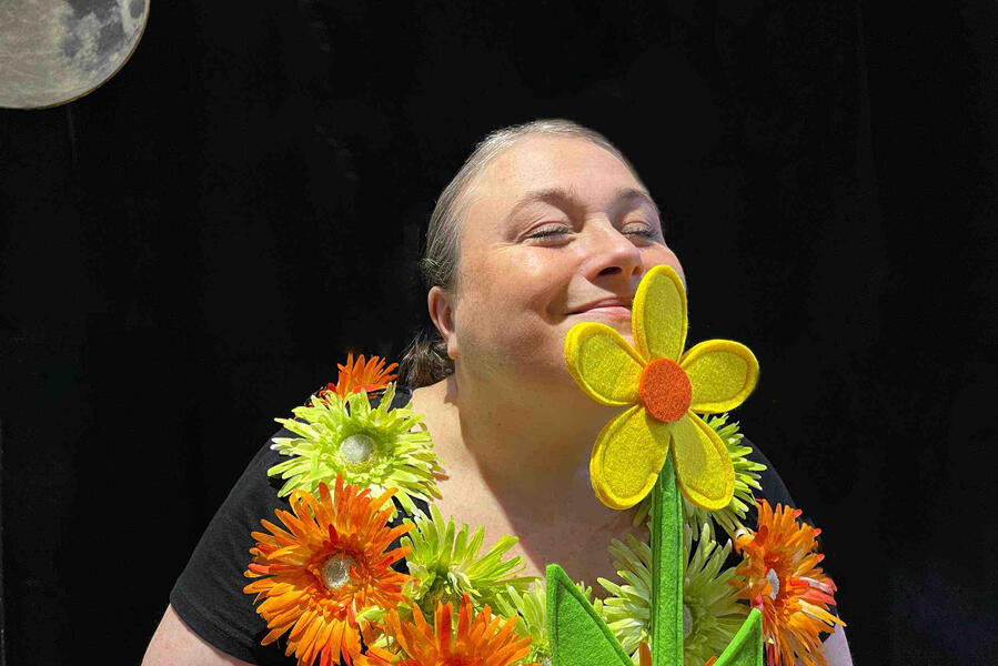 J'me cache ! Photo d’Aurore en pleine représentation, entourée de son décor de spectacle avec ses fleurs.