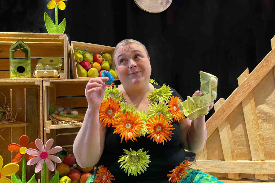 J'me cache ! Décor de spectacle : Aurore la comédienne avec son costume, tout en fleurs et son décor, tout en bois tient sa main, un oeuf en levant les yeux vers le clair de Lune.