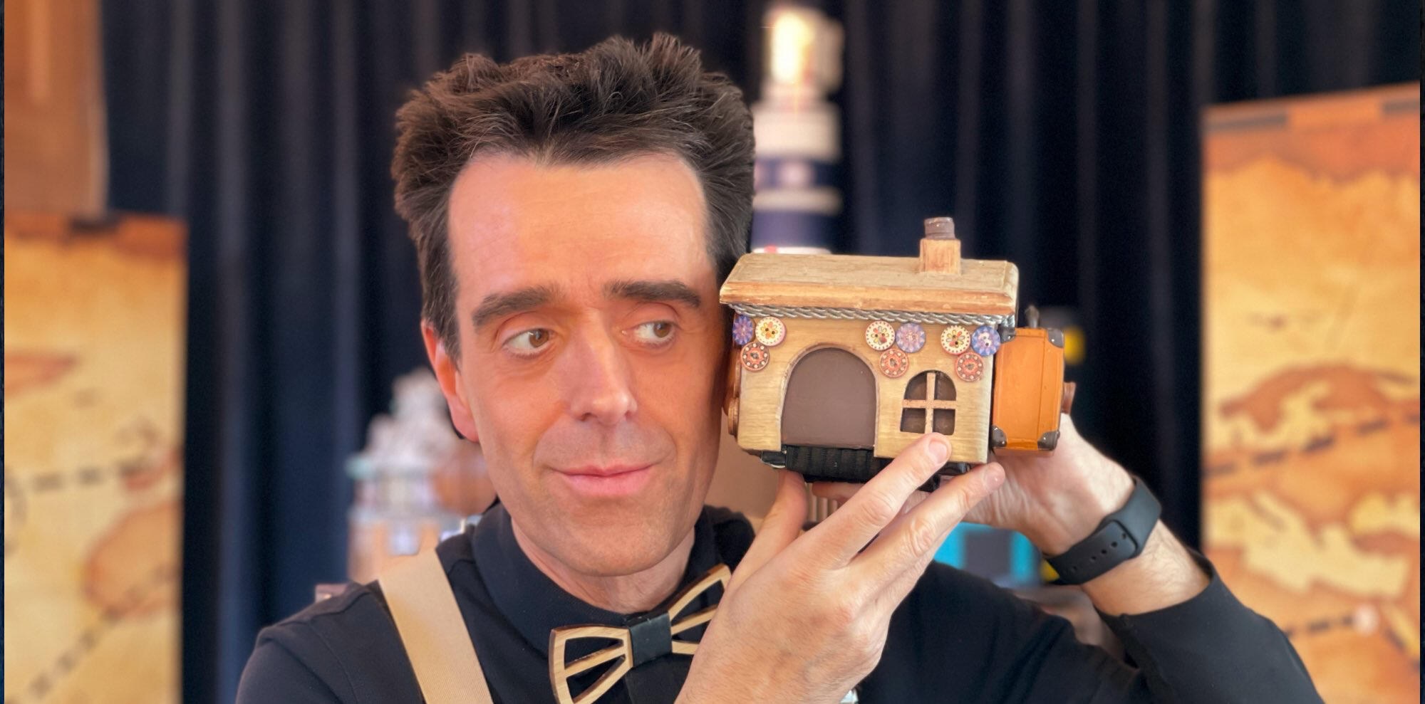 Monsieur Fred sur scène avec le décor de l’île et du village, présentant le spectacle “Risque-Tout” pour jeunes enfants.
